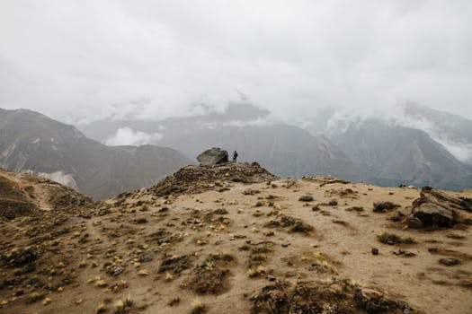 A lone figure standing on a rugged mountain amidst misty clouds at dawn.