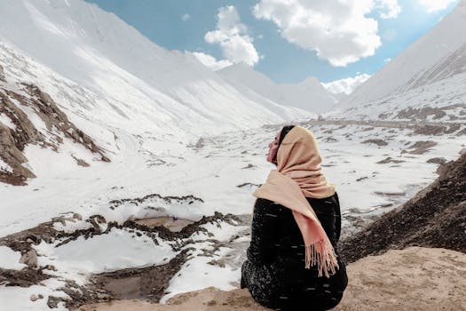 A woman sits on a snowy mountain, wrapped in a scarf, enjoying the serene winter view.