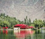 Stunning lake view with traditional architecture and vibrant red roofs framed by mountains and trees.
