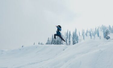 A man leaps across a snow-covered hillside against a backdrop of trees in Gulmarg.