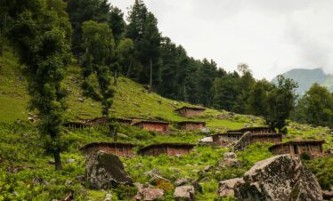 Charming rural village nestled in lush mountains with scattered stone cottages and dense forests.