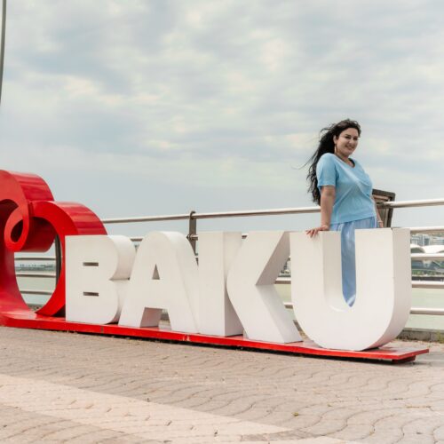 A woman poses by the iconic Baku sign overlooking the bay, showcasing city charm.