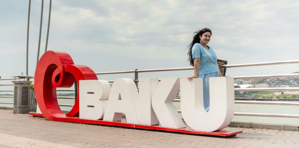 A woman poses by the iconic Baku sign overlooking the bay, showcasing city charm.