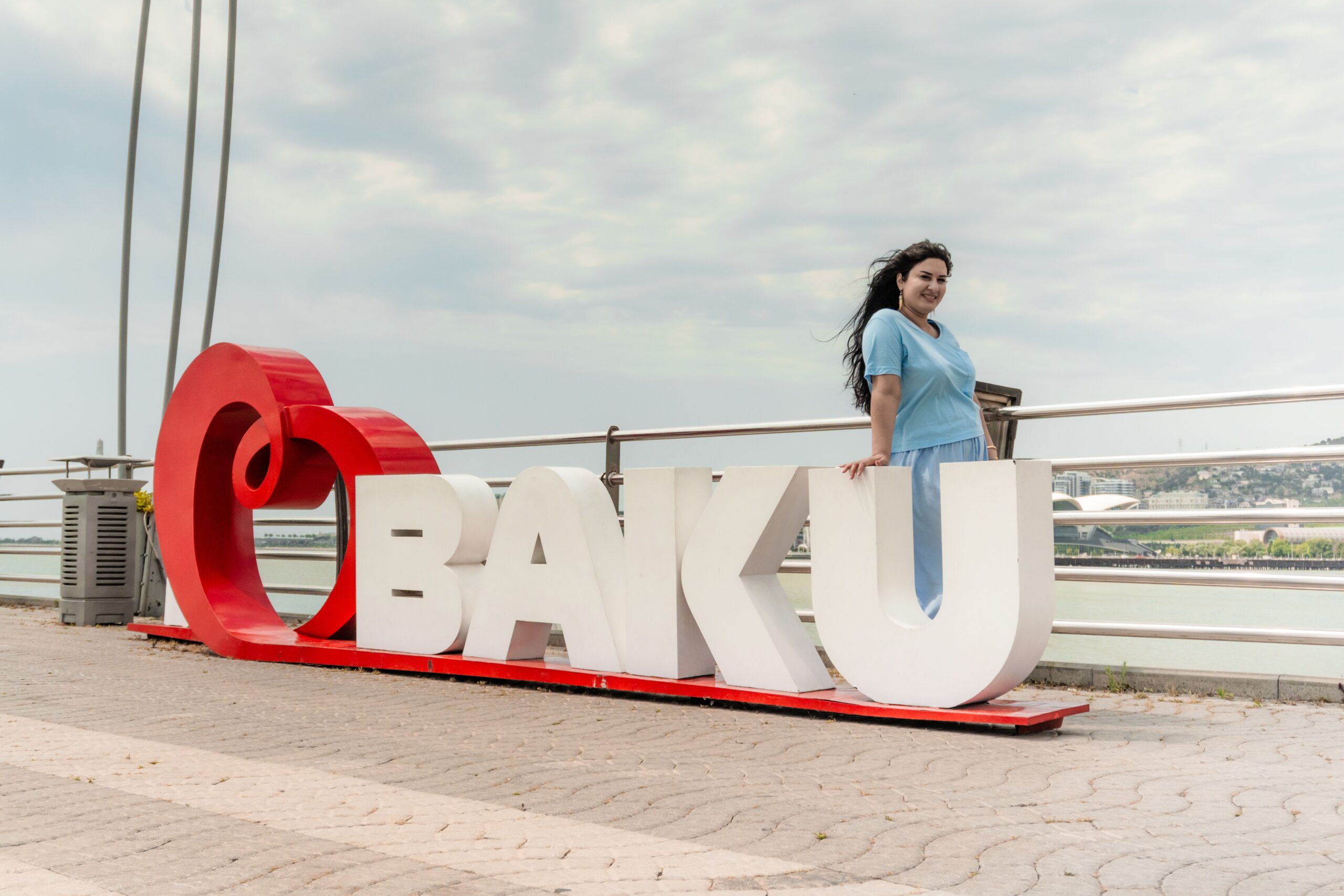 A woman poses by the iconic Baku sign overlooking the bay, showcasing city charm.
